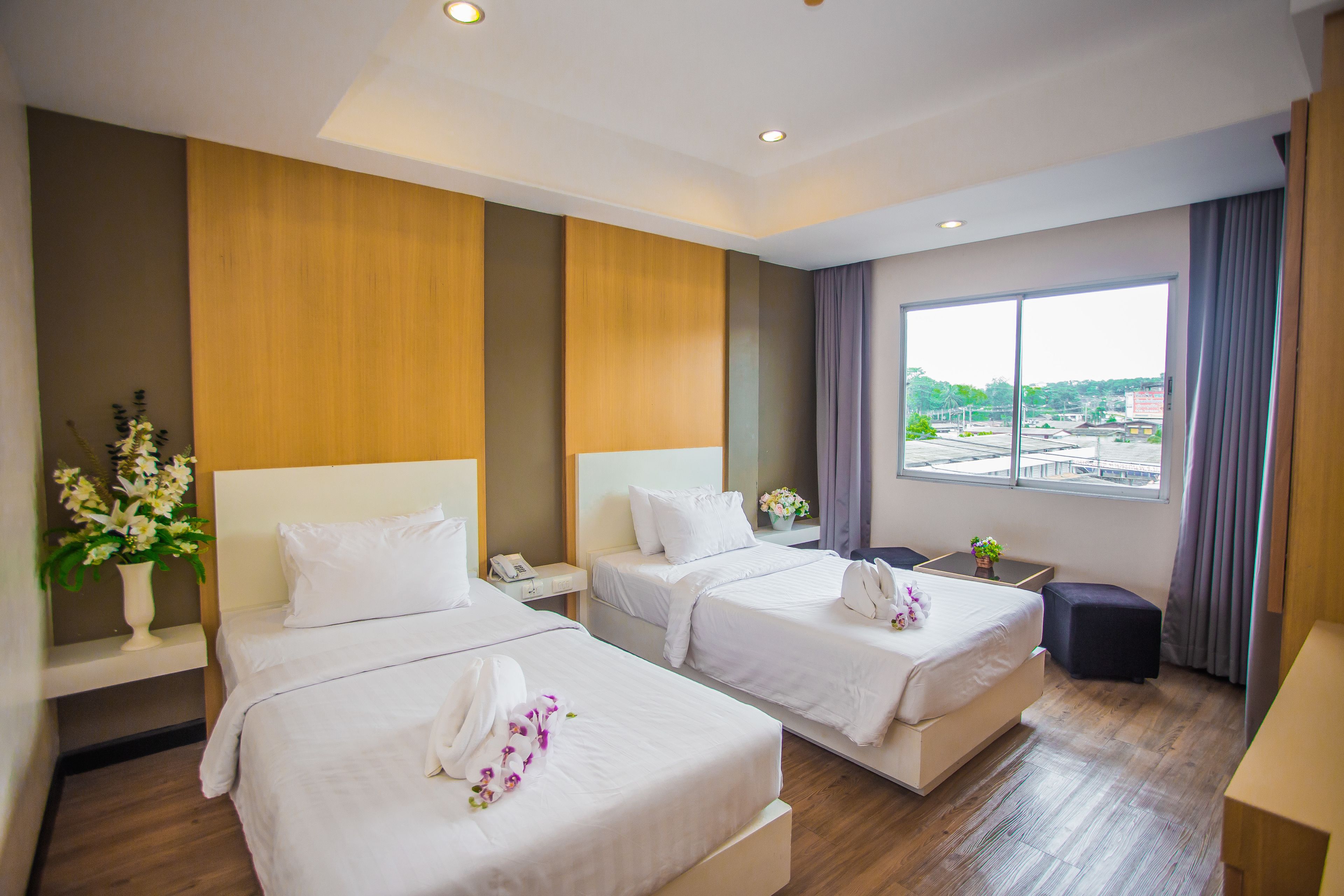 A hotel room with two beds, a small desk, a chair, a nightstand, and a window with a view of the city.