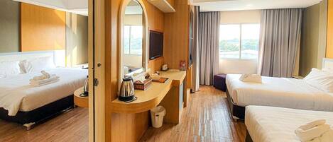 Habitación de hotel con dos camas, un escritorio con televisor y vistas al exterior.