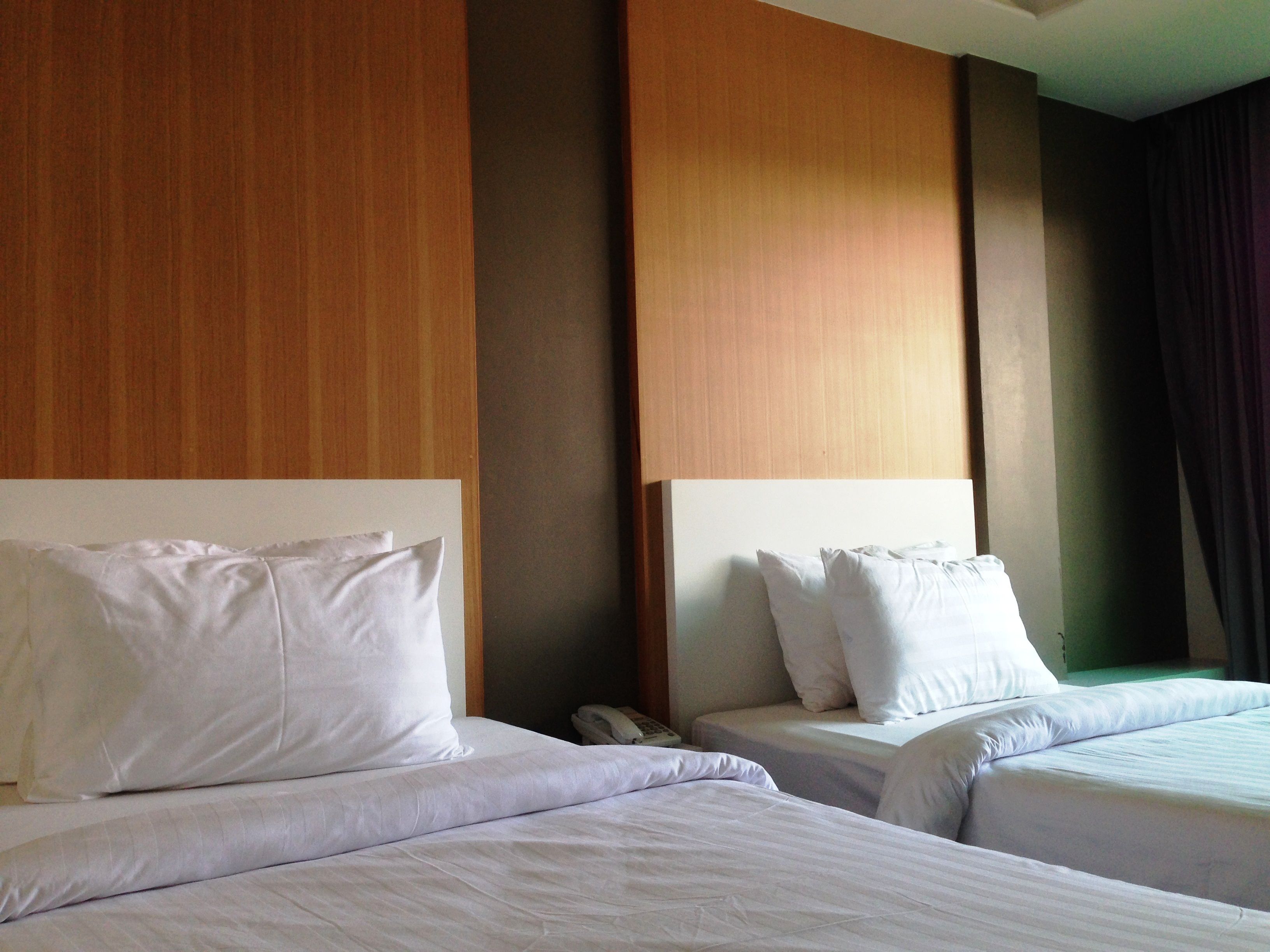 A hotel room with two beds, each with white linens and pillows. There is a telephone on the nightstand next to one bed. The room has wooden paneling on the walls and a green accent wall.
