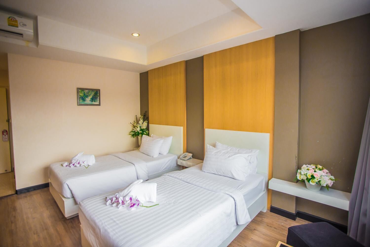 A hotel room with two beds, a bedside table, a small desk, a telephone, and a flower arrangement.