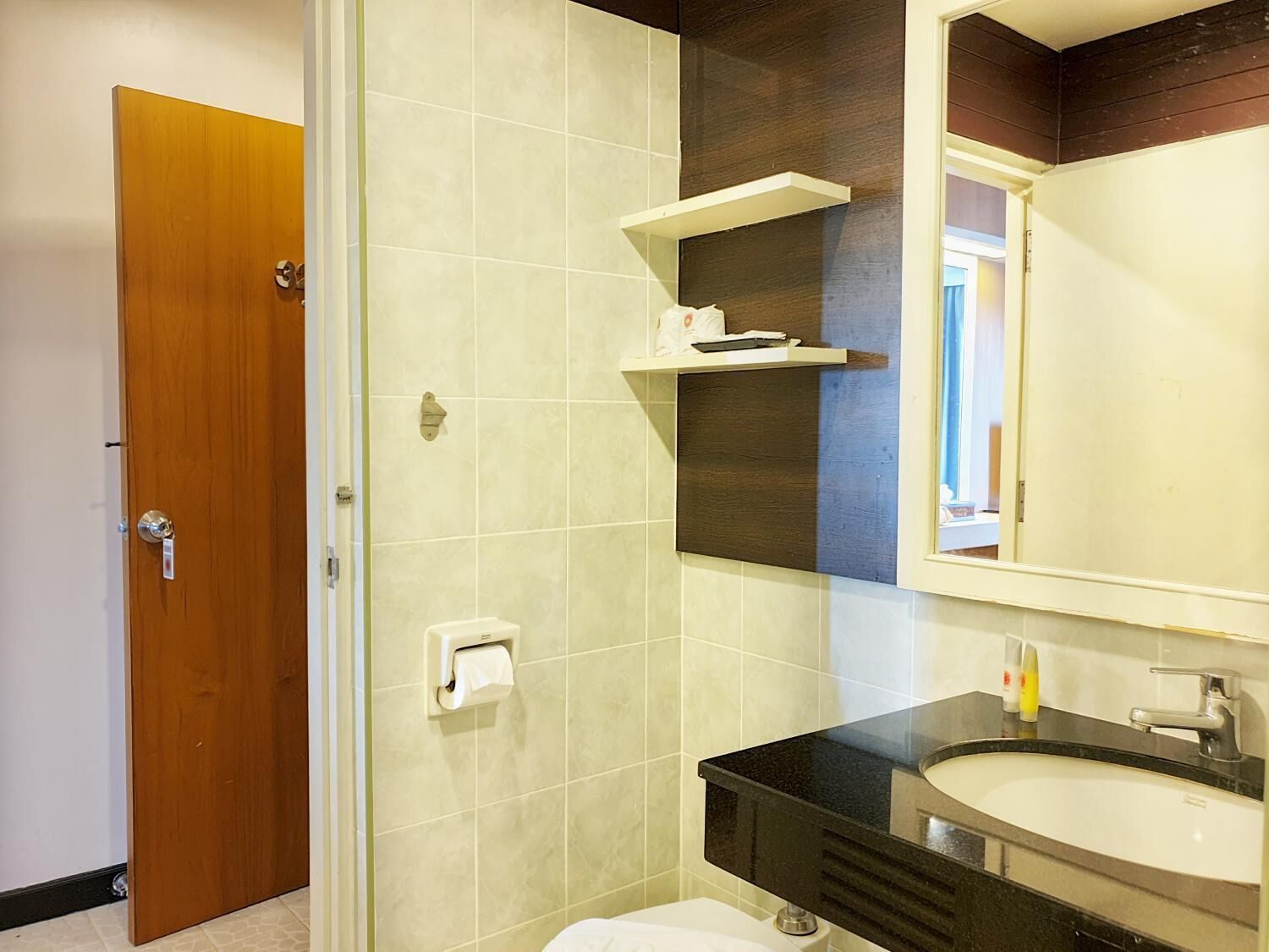A bathroom with a wooden door, a toilet paper holder, a mirror, and a sink with a black countertop.