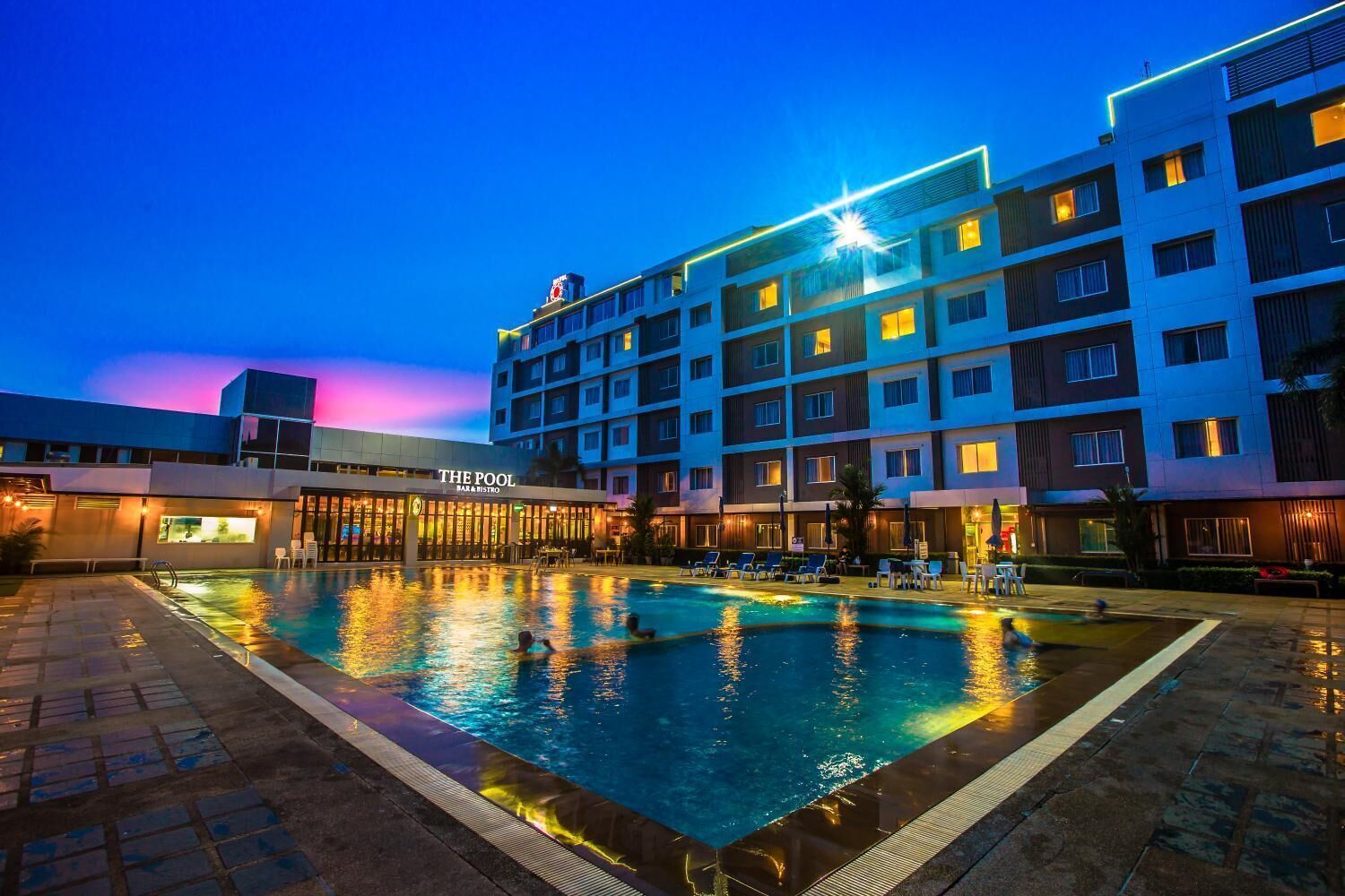 Un hôtel doté d’une piscine, d’un bar et d’un restaurant, ainsi que d’un immeuble à plusieurs étages dont les fenêtres sont illuminées.