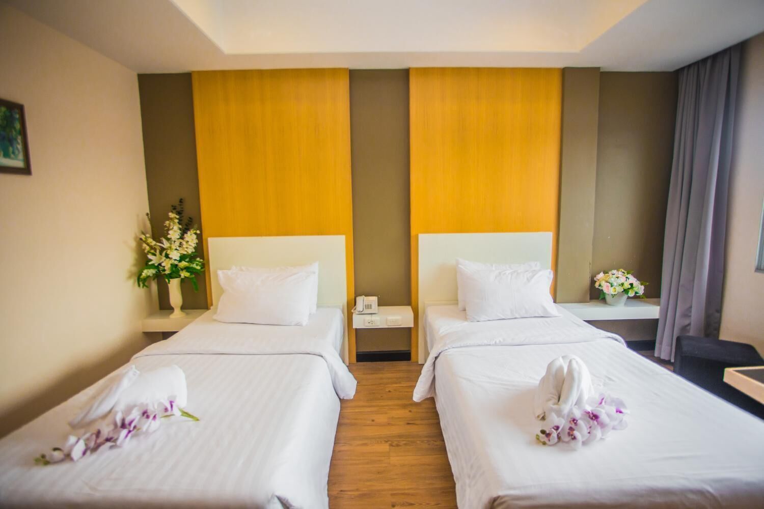 A hotel room with two beds, a nightstand with a phone, and a vase with flowers.