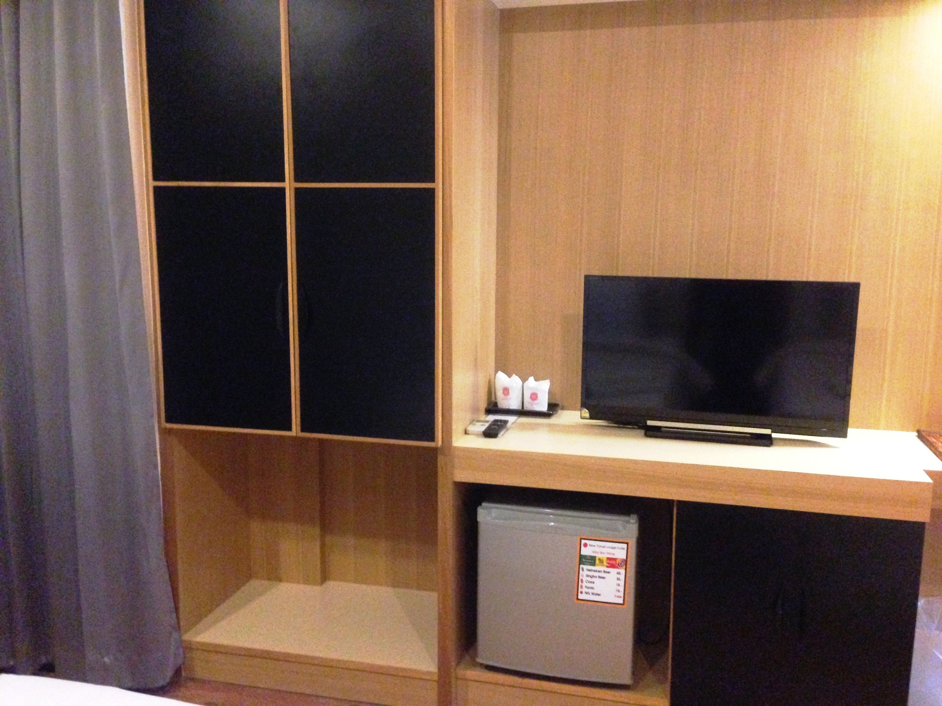 Habitación de hotel con una televisión sobre un escritorio de madera, un refrigerador pequeño y una cortina.