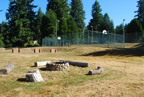 A fenced outdoor area with a basketball court, a small building, and a forested background.