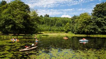A calm lake with kayaks and a canoe, surrounded by dense greenery and trees.