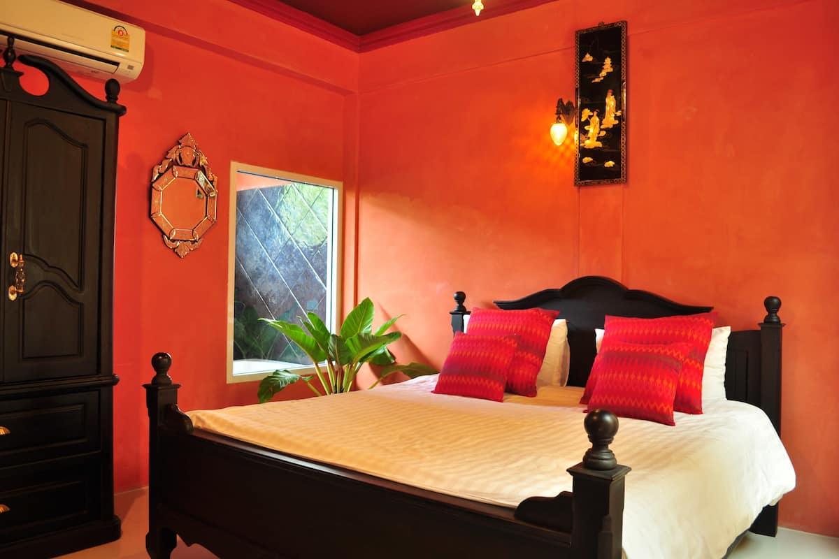A bedroom with a bed, a window, a plant, and a wall-mounted air conditioner.