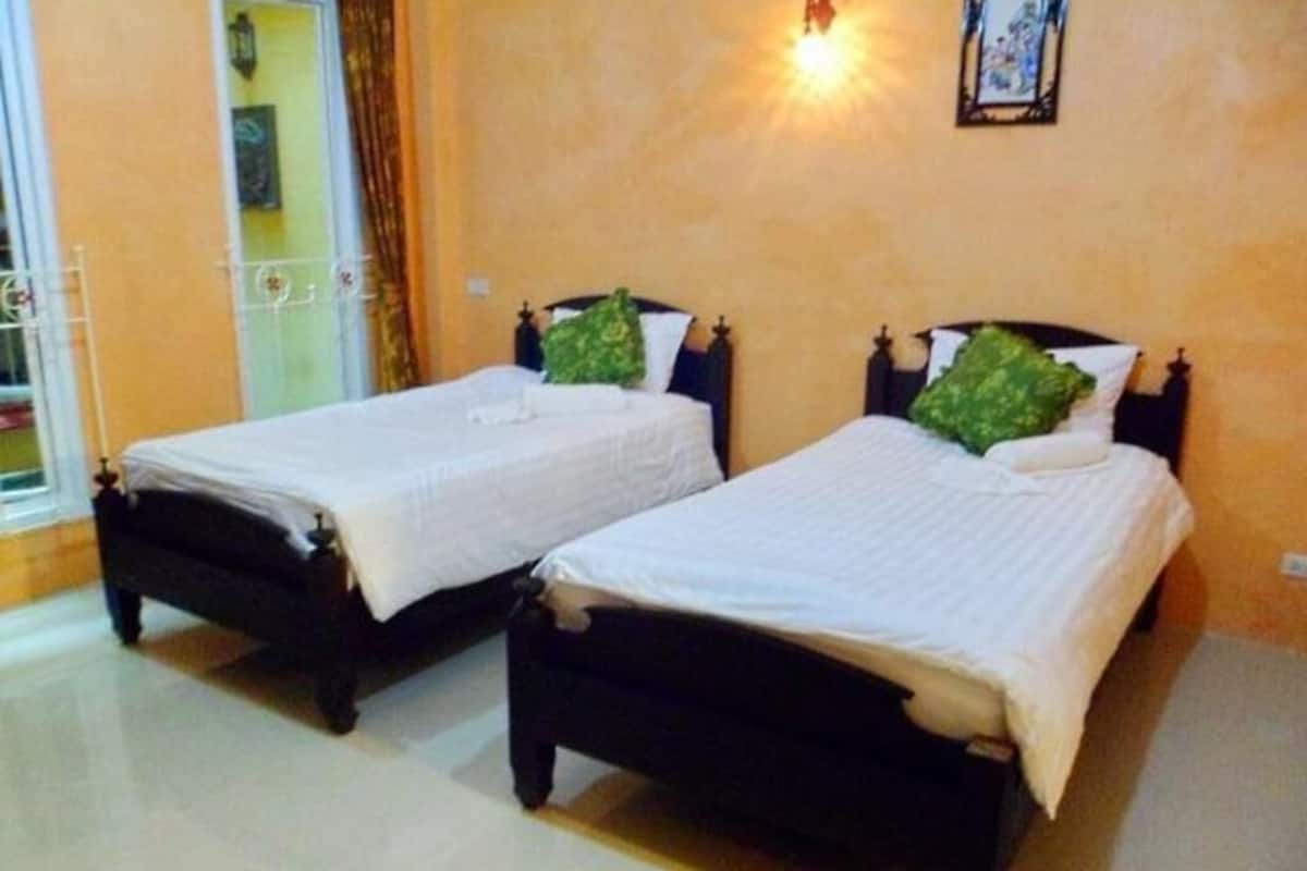Two single beds with dark frames and green pillows, a wall-mounted light fixture, and a door with a metal gate.