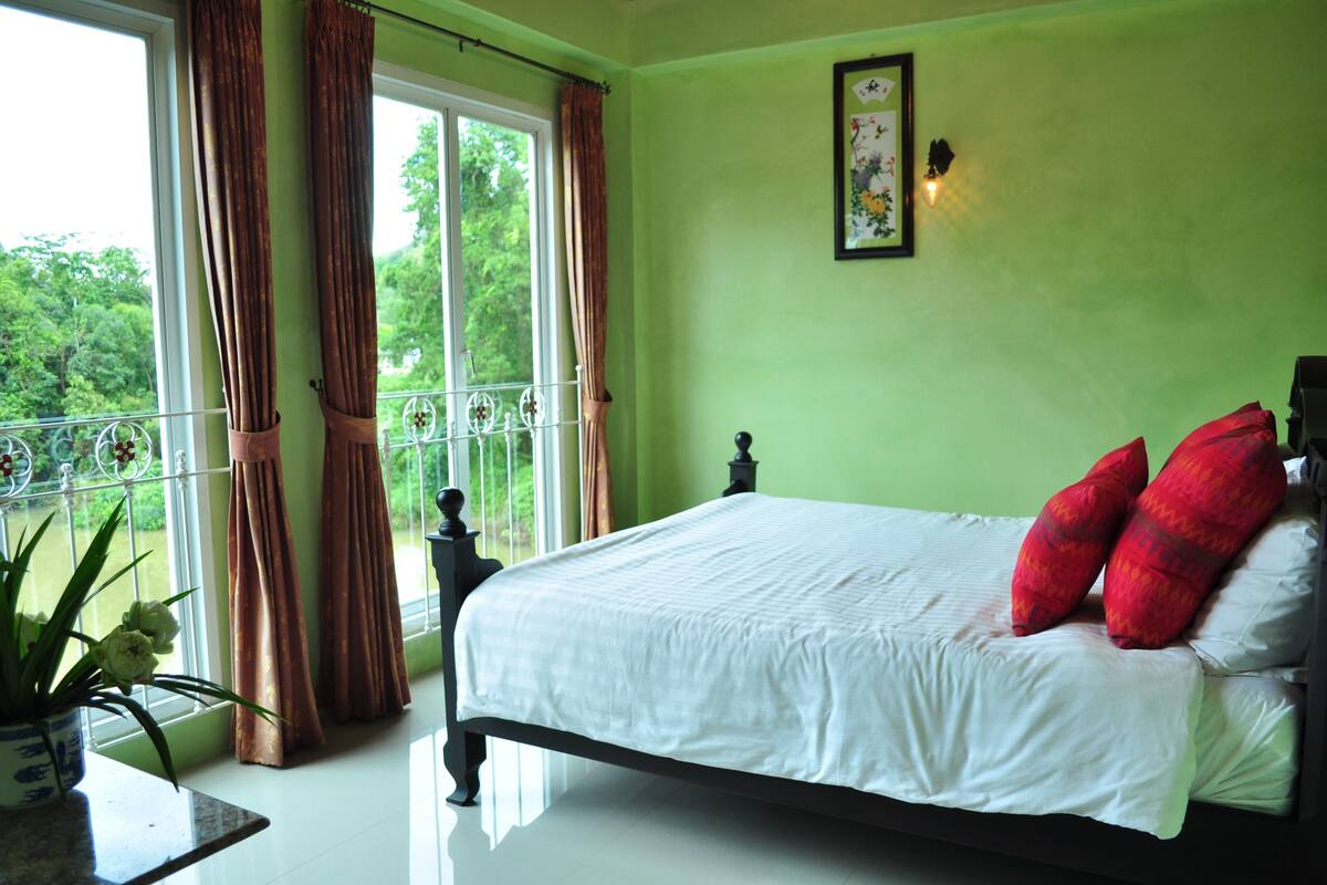 A bedroom with a bed, green walls, a window with curtains, and a balcony.