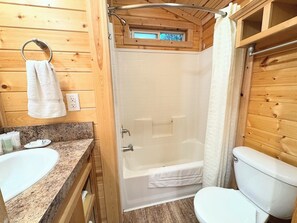 A wooden cabin bathroom with a shower, toilet, and granite countertop sink.