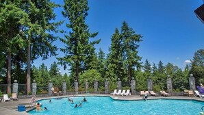 A swimming pool surrounded by tall trees, with lounge chairs and a stone wall. - Tall Chief RV & Camping Resort (Fall City)