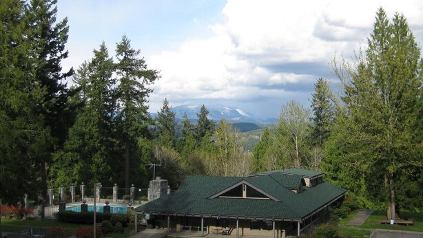 A lodge with a green roof, a swimming pool, and a view of mountains. - Tall Chief RV & Camping Resort (Fall City)