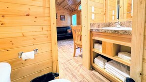 A wooden cabin interior with a bathroom featuring a toilet, sink, and shelves with towels. - Tall Chief RV & Camping Resort (Fall City)