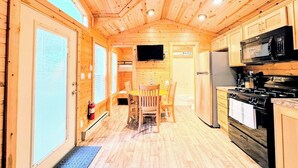 A wooden cabin interior with a kitchen, dining area, and a television mounted on the wall. - Tall Chief RV & Camping Resort (Fall City)