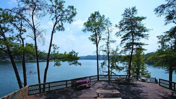 A wooden deck with picnic tables overlooking a lake surrounded by trees. - Hidden Cove RV Resort (Arley)