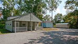 A two-story cabin with a porch and a small deck, surrounded by trees and a gravel driveway. - Hidden Cove RV Resort (Arley)