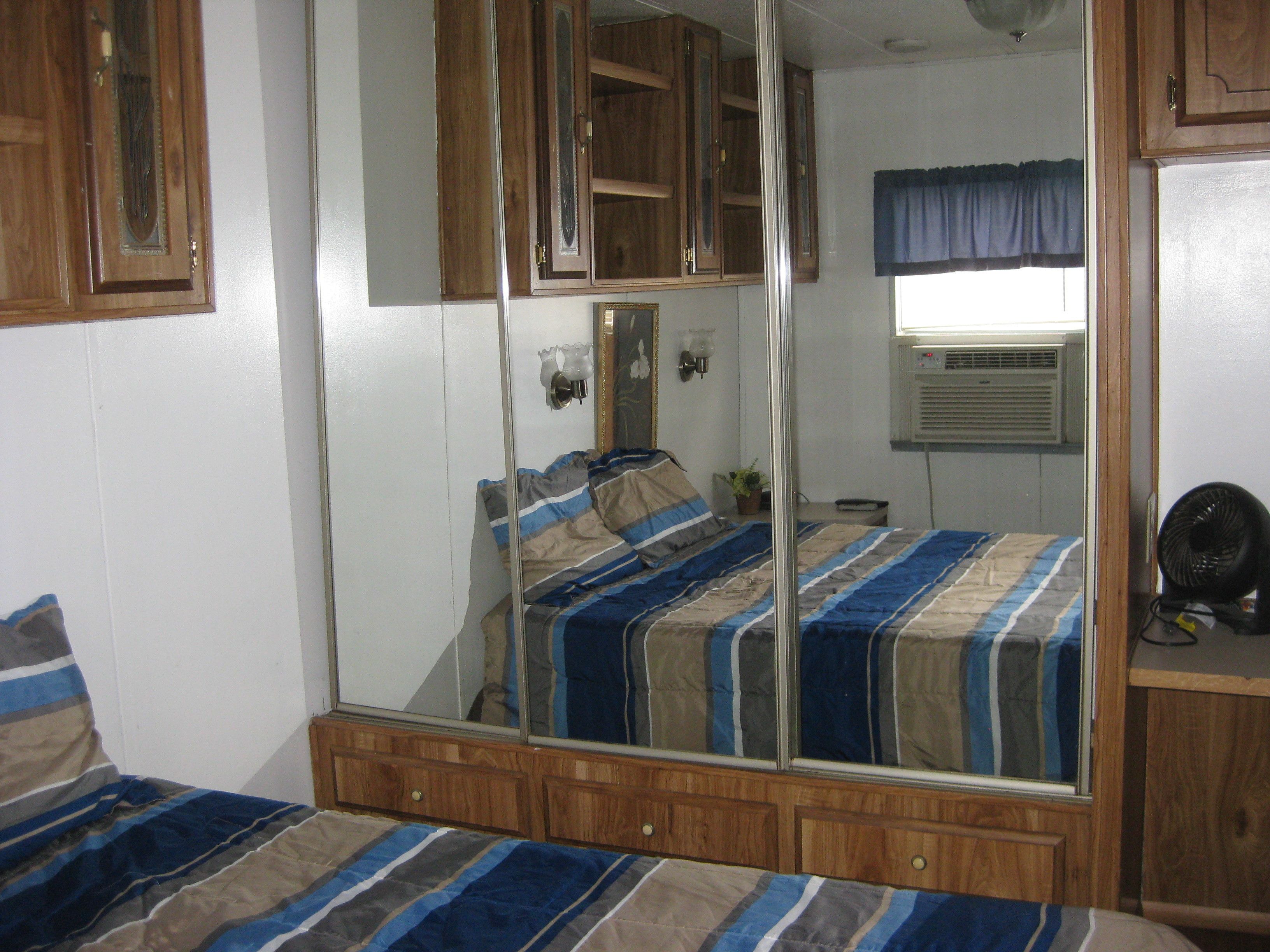 A bedroom with a large mirror, a bed with striped bedding, wooden furniture, and a window with a curtain.