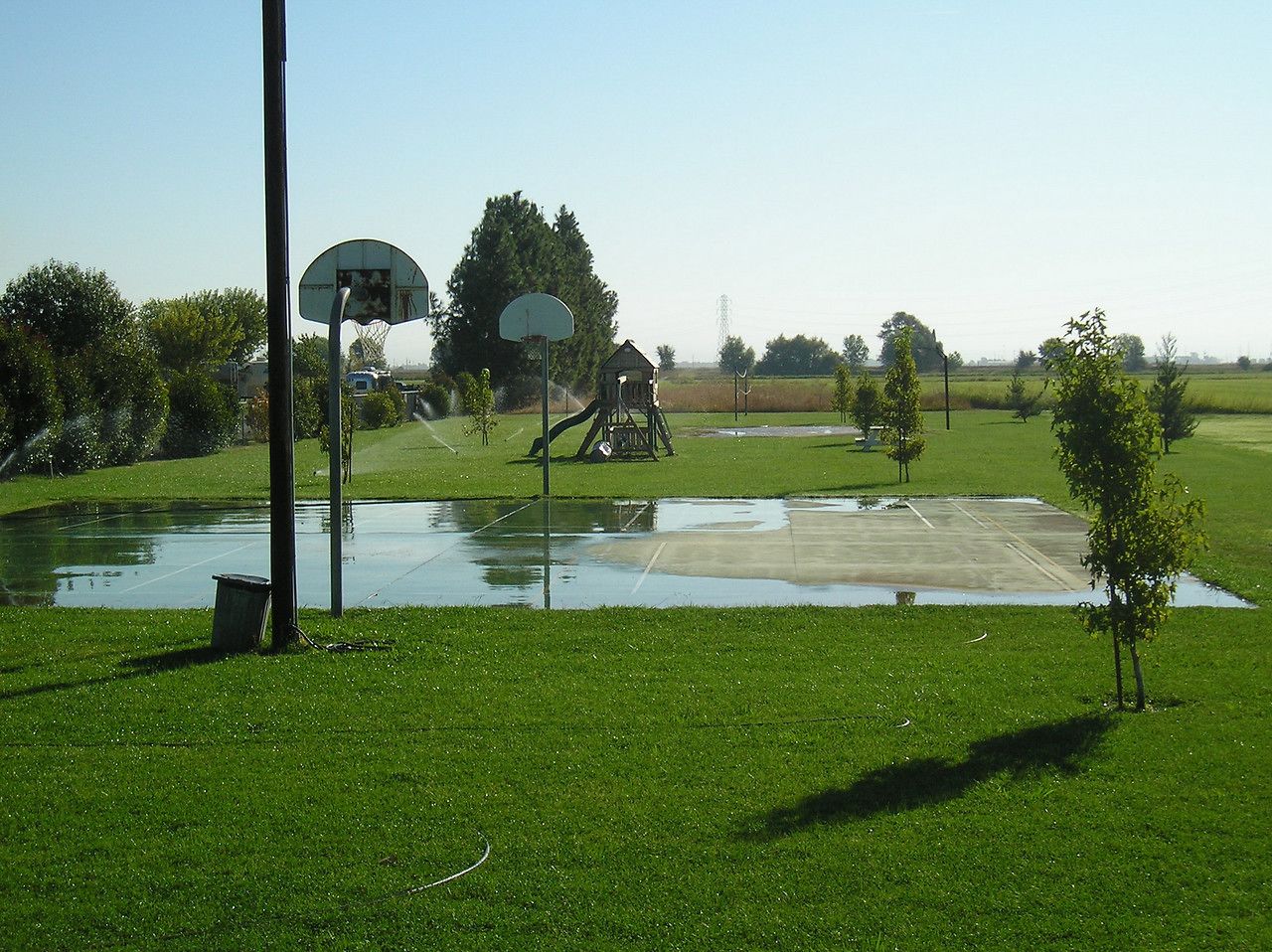 A basketball court with a hoop and a small shed in a grassy area.