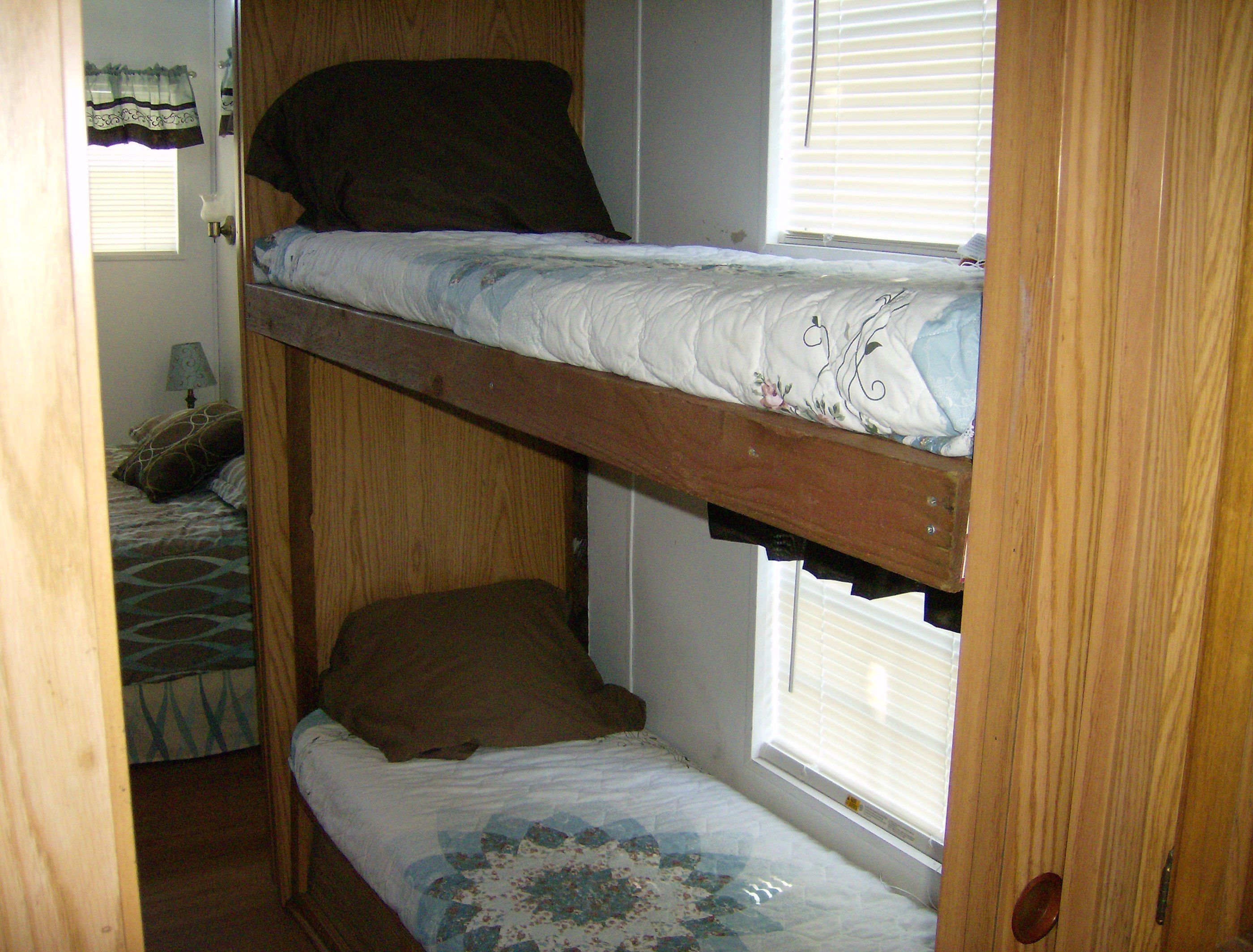 A bunk bed with a lower bunk, a window with blinds, and a door with a curtain.
