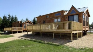 A row of wooden cabins with deck access, surrounded by a grassy area and trees. - Lakeland RV Campground (Milton)