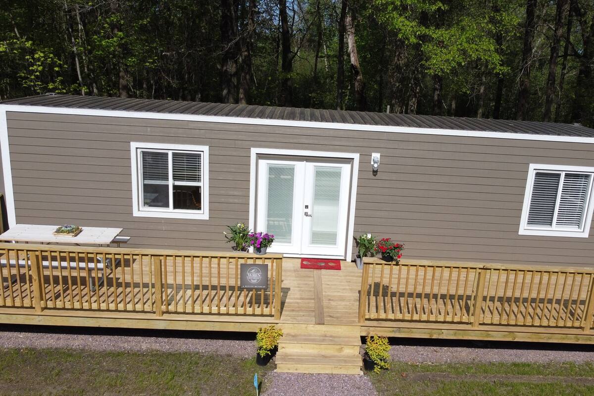 A single-story mobile home with a front deck, two windows, a door, and a small porch area.