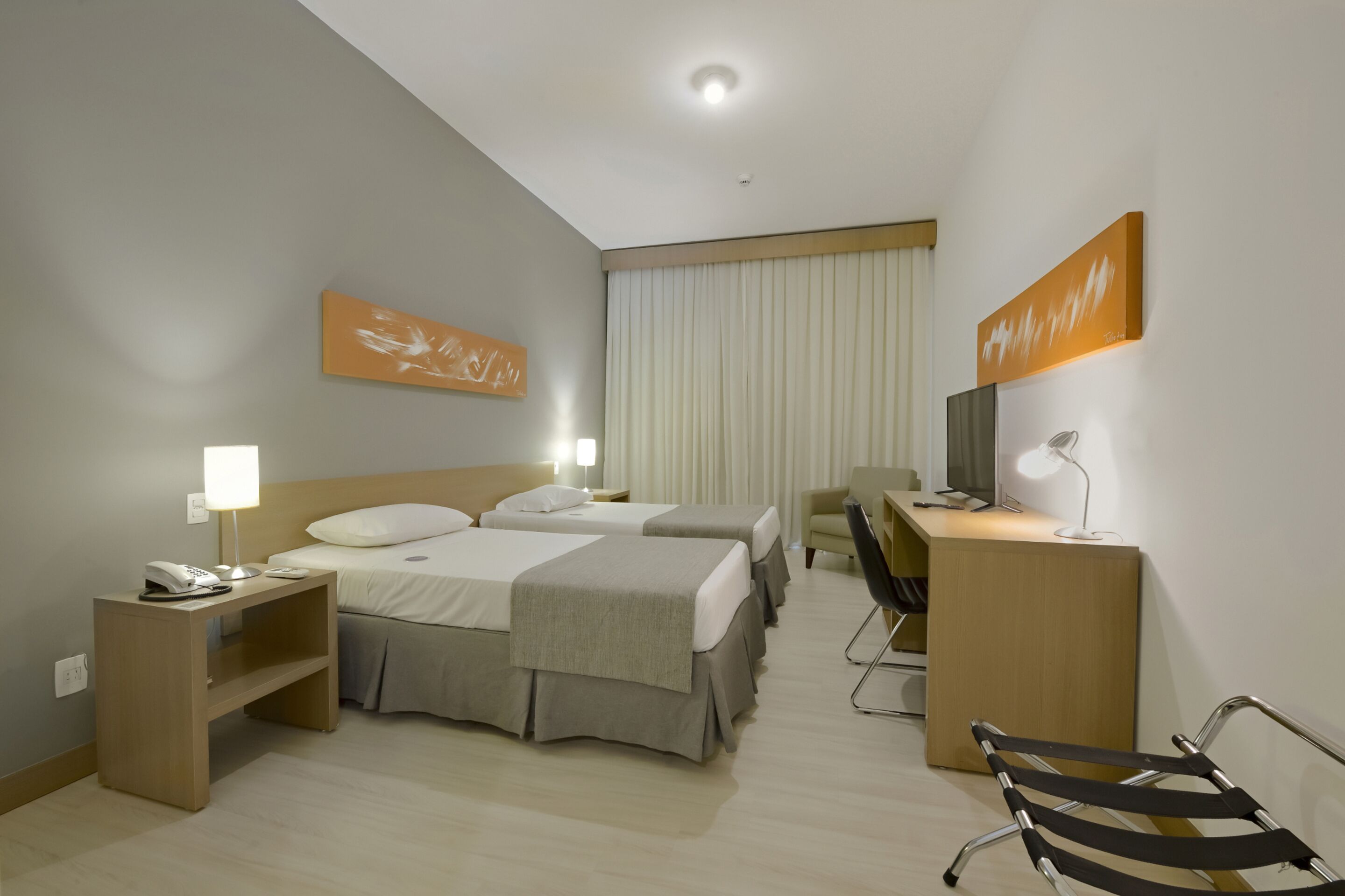 Habitación de hotel con dos camas, un escritorio, una silla y un televisor.
