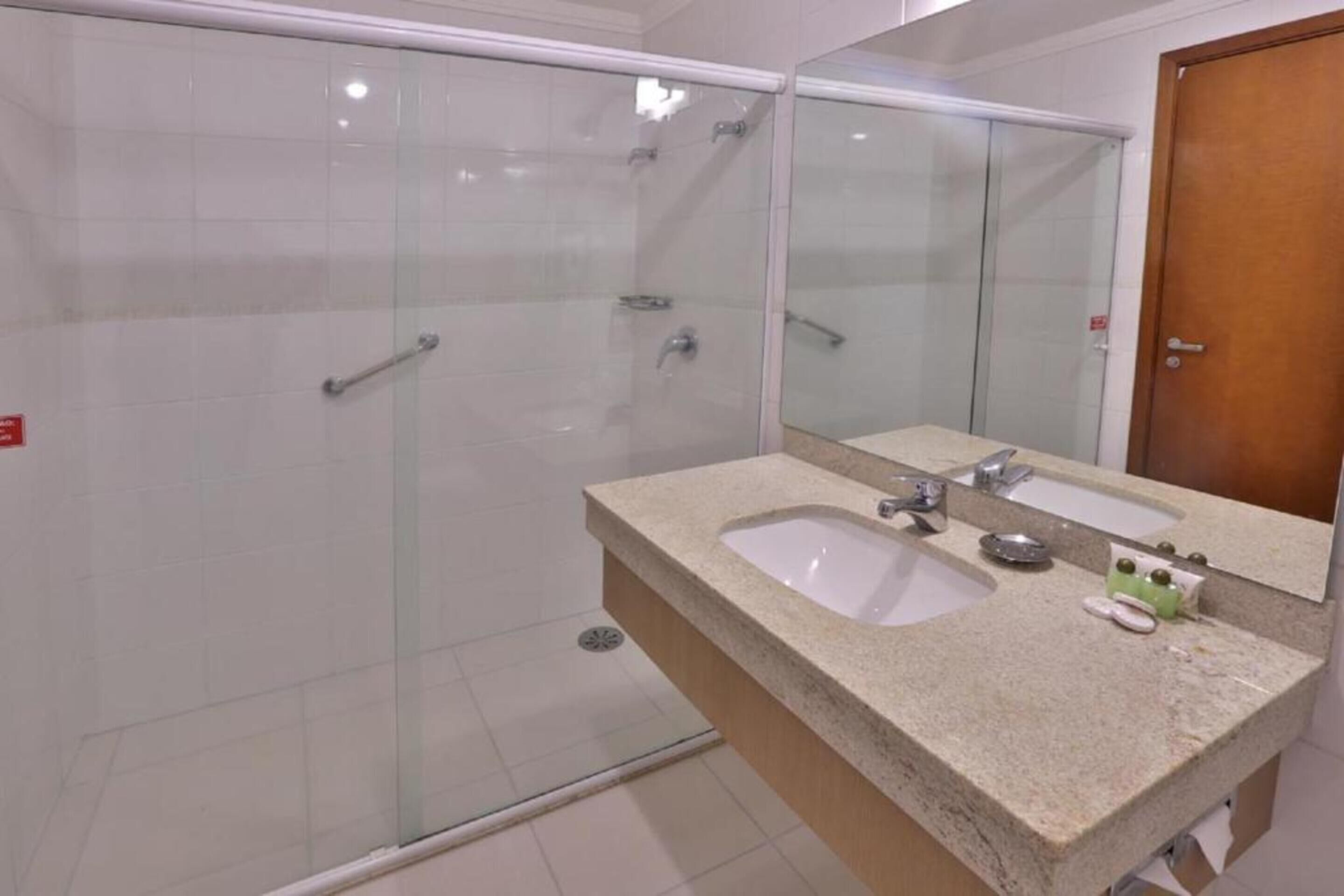 A bathroom with a glass shower enclosure, a granite countertop, two sinks, and a mirror.