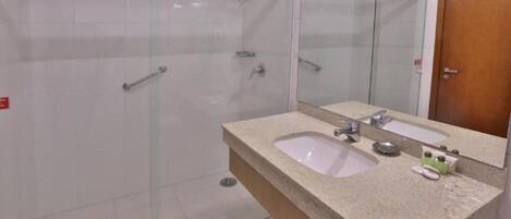A bathroom with a glass shower enclosure, a granite countertop, two sinks, and a mirror.
