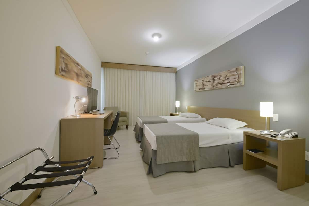 Ein Hotelzimmer mit zwei Betten, einem Schreibtisch, einem Stuhl, einem Nachttisch mit Lampe und Bildern an den Wänden.