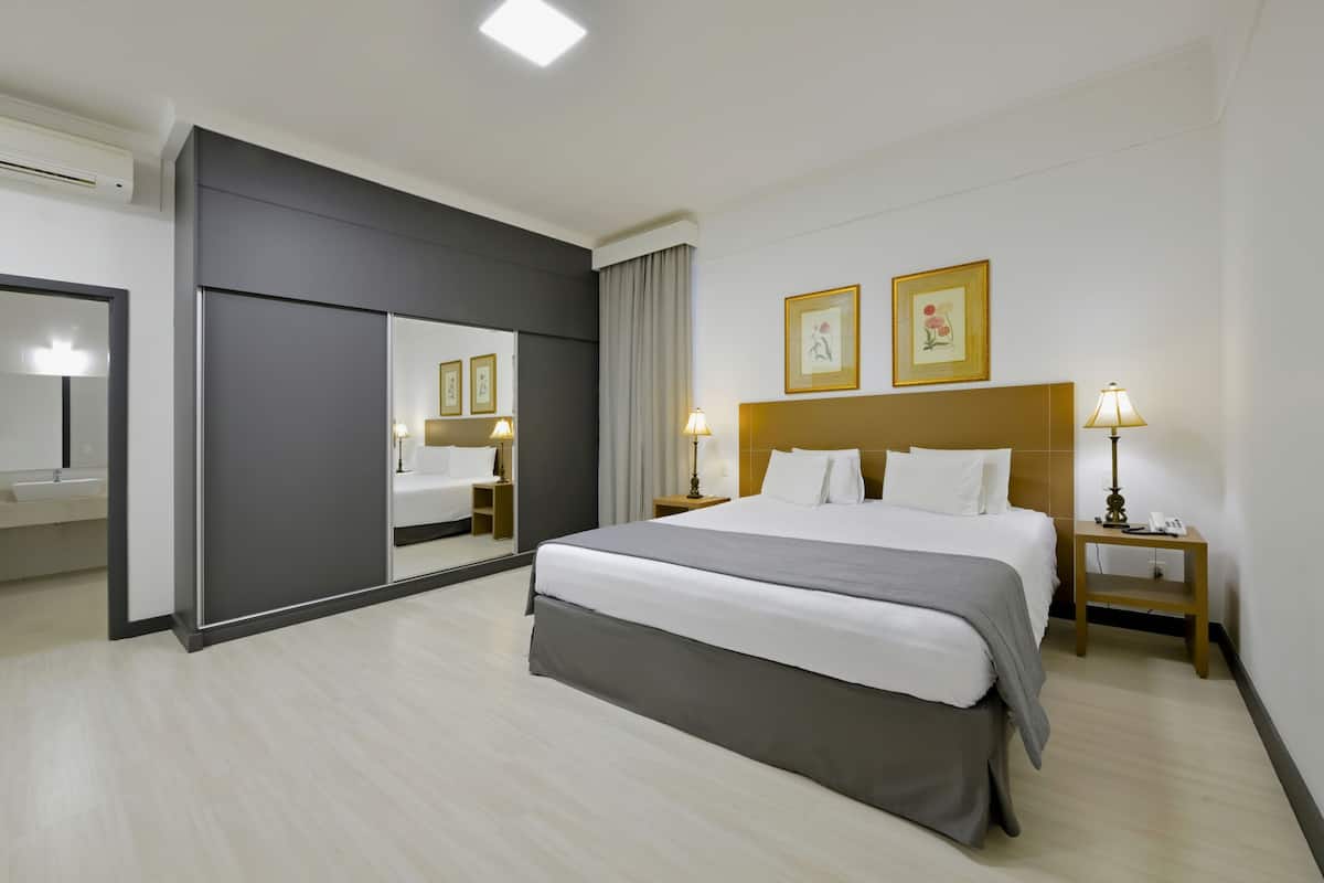 Ein modernes Hotelzimmer mit einem großen Bett, einem Nachttisch mit Lampe, einem Spiegel und zwei gerahmten Bildern an der Wand.