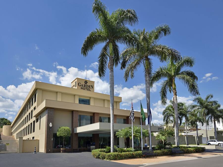 A hotel with a modern design, featuring a prominent entrance, palm trees, and a clear blue sky.