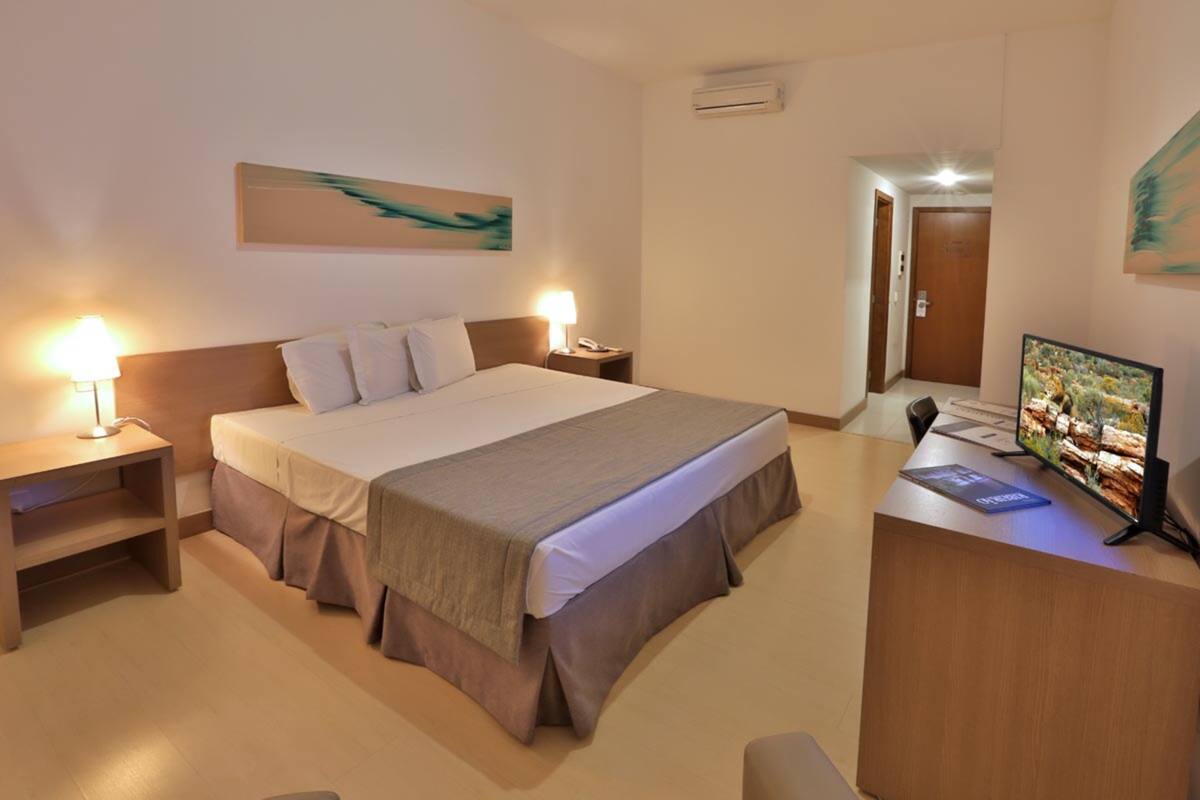 Ein Hotelzimmer mit einem Bett, Nachttischen, einem Schreibtisch mit Computer und einem Fernseher.