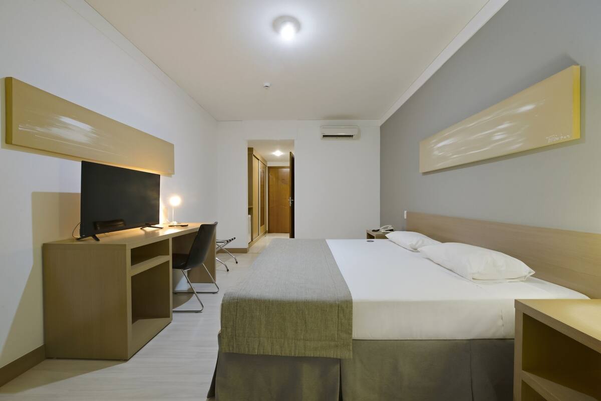 Ein Hotelzimmer mit einem Bett, einem Schreibtisch mit Stuhl, einem Fernseher und einem Nachttisch.