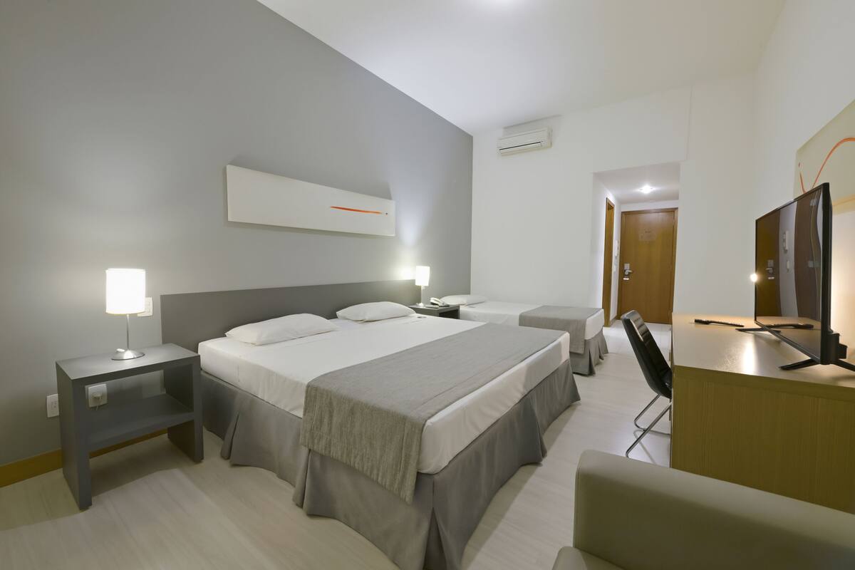 Ein modernes Hotelzimmer mit einem großen Bett, Nachttischen, einem Schreibtisch und einem Fernseher.