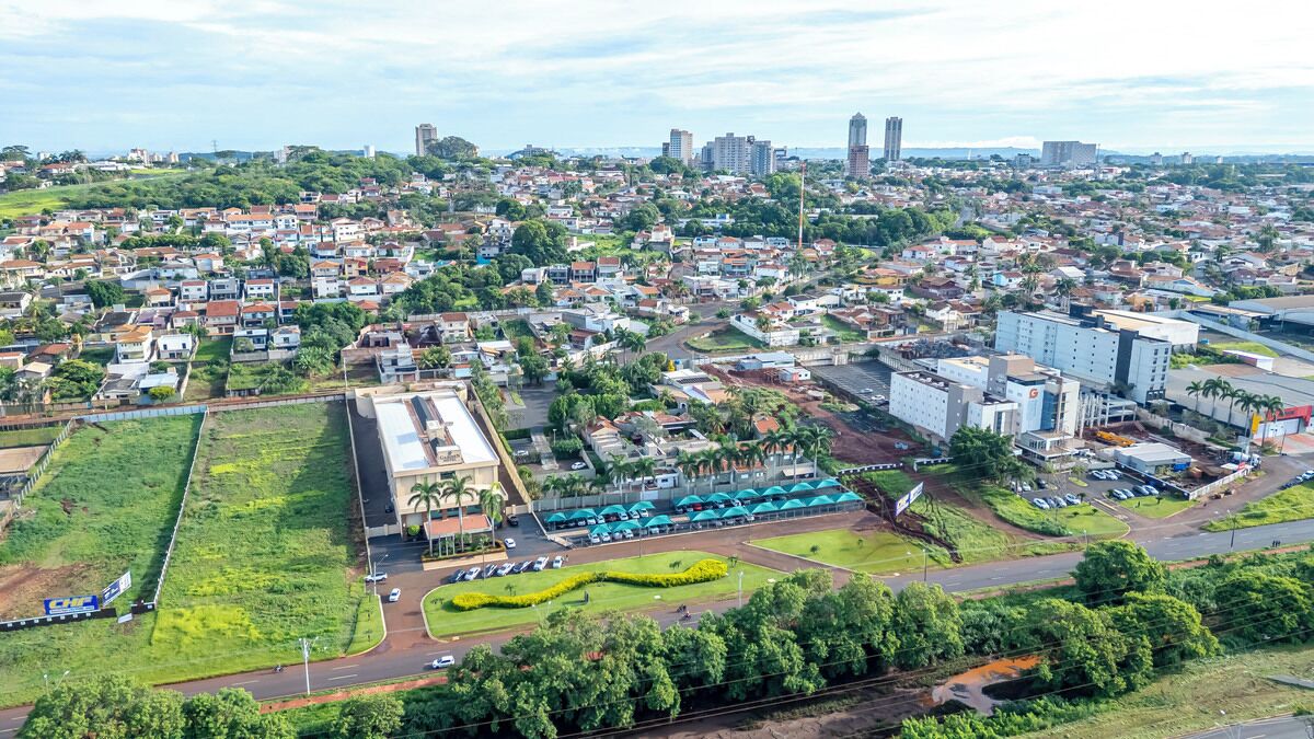 Vista aérea de un paisaje urbano con zonas residenciales, edificios comerciales y un amplio estacionamiento con toldos azules.