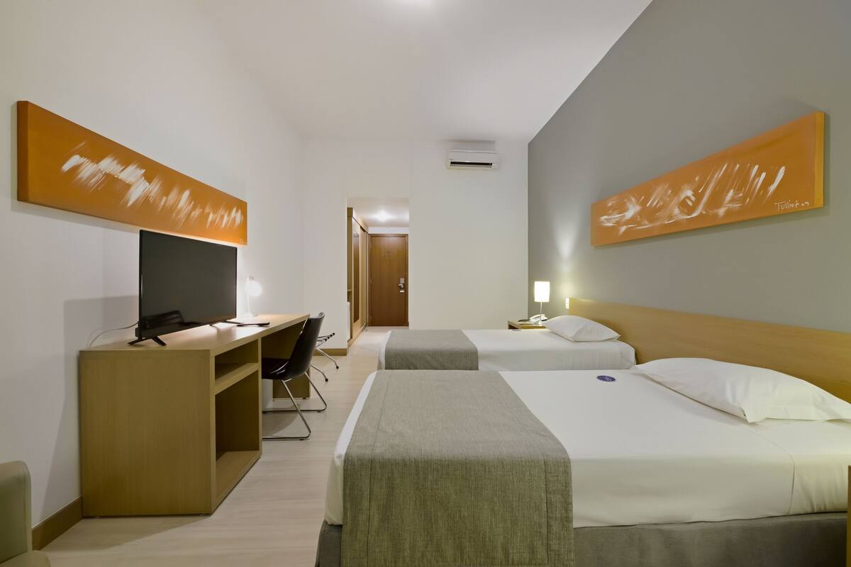 Ein Hotelzimmer mit zwei Betten, einem Schreibtisch mit Fernseher und Bildern an den Wänden.