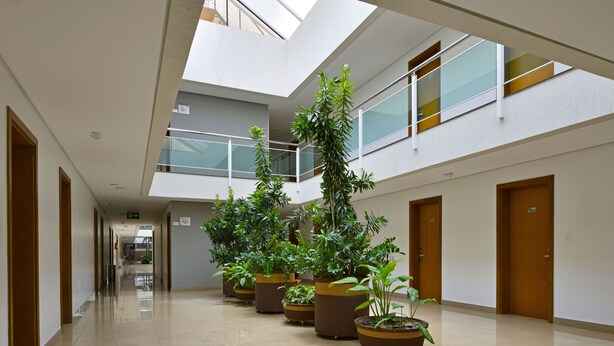 A modern building with a central atrium, multiple floors, and potted plants. - Garden Hotel (Ribeirão Preto)