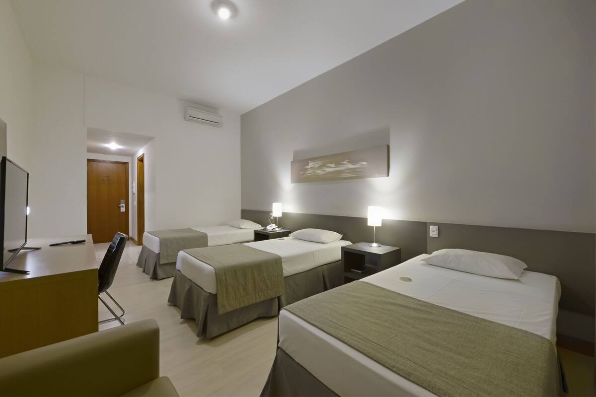 Ein Hotelzimmer mit zwei Einzelbetten, einem Schreibtisch mit Stuhl, einem Fernseher und einem kleinen Tisch.