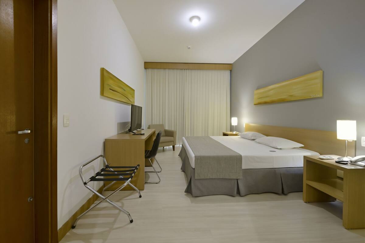 Ein Hotelzimmer mit Bett, Schreibtisch, Stuhl und Nachttisch mit Lampe.