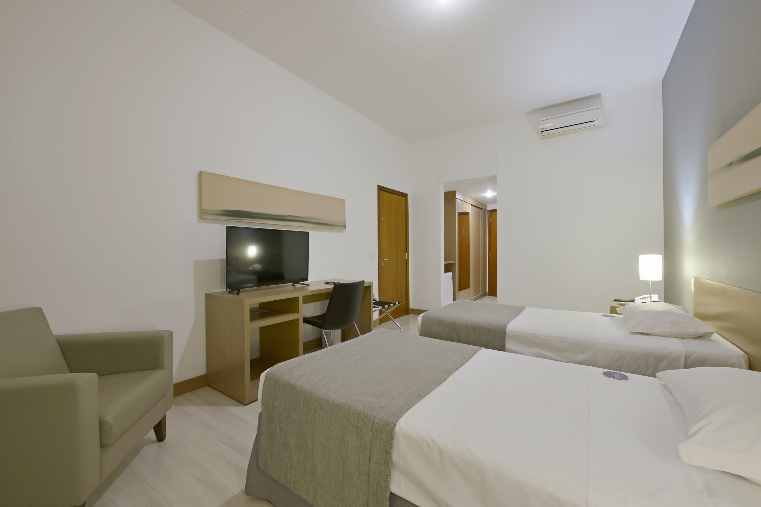 A hotel room with two beds, a desk with a chair, a television, and a sofa.