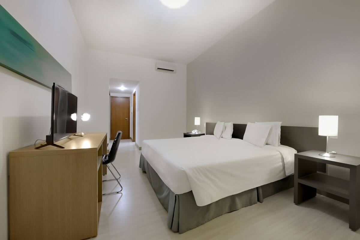 Ein Hotelzimmer mit Bett, Nachttischen, Schreibtisch, Stuhl und Fernseher.