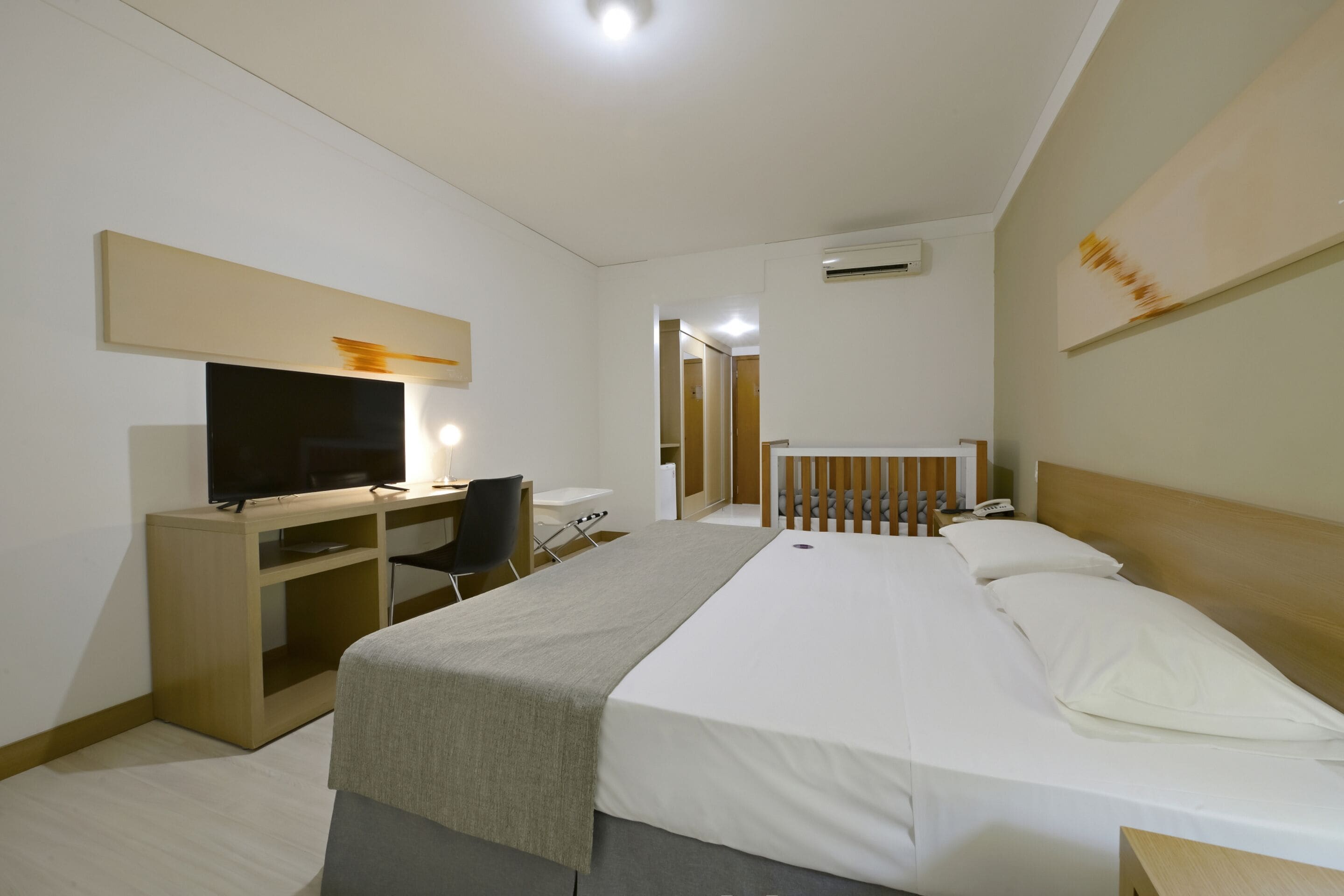 Una habitación de hotel con una cama, un escritorio con computadora, un televisor y una mesita de noche.