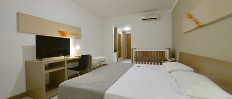 Una habitación de hotel con una cama, un escritorio con computadora, un televisor y una mesita de noche.