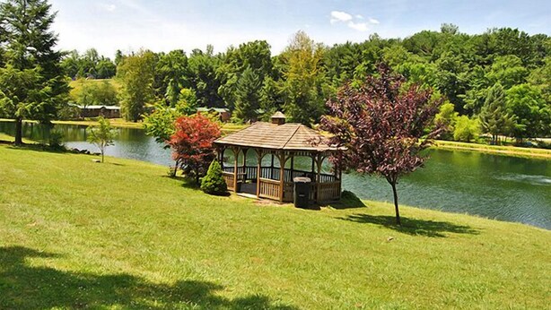 A gazebo by a lake with a well-maintained lawn and trees.