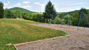 A playground with a swing set and a sandbox in a grassy area with trees and hills in the background.