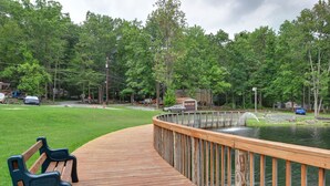 A wooden deck with a bench, overlooking a lake with a wooden dock and a small building in the background. - Sun Valley Camping and RV Resort (Narvon)