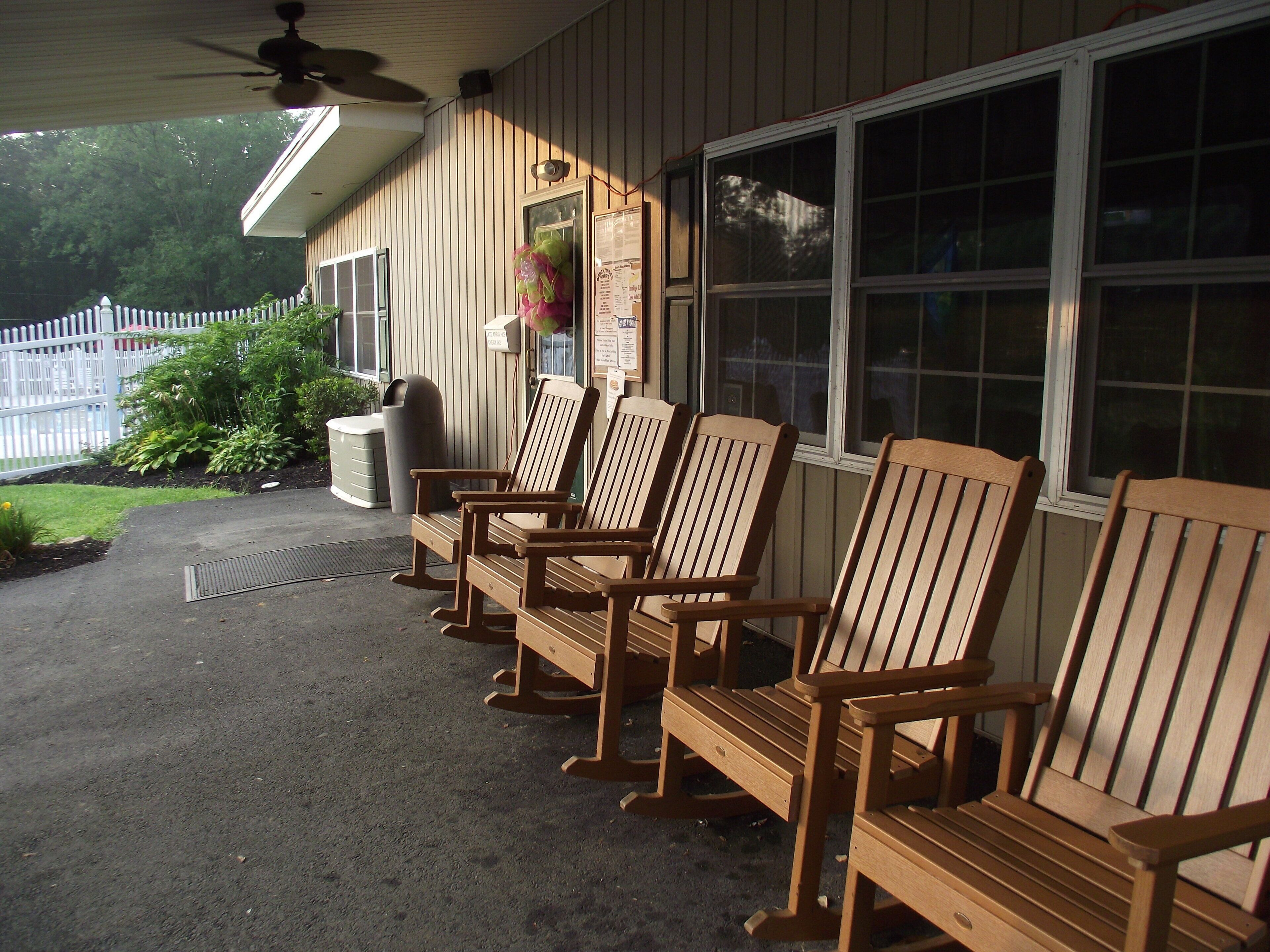 A row of wooden Adirondack chairs on a porch with a white picket fence in the background.