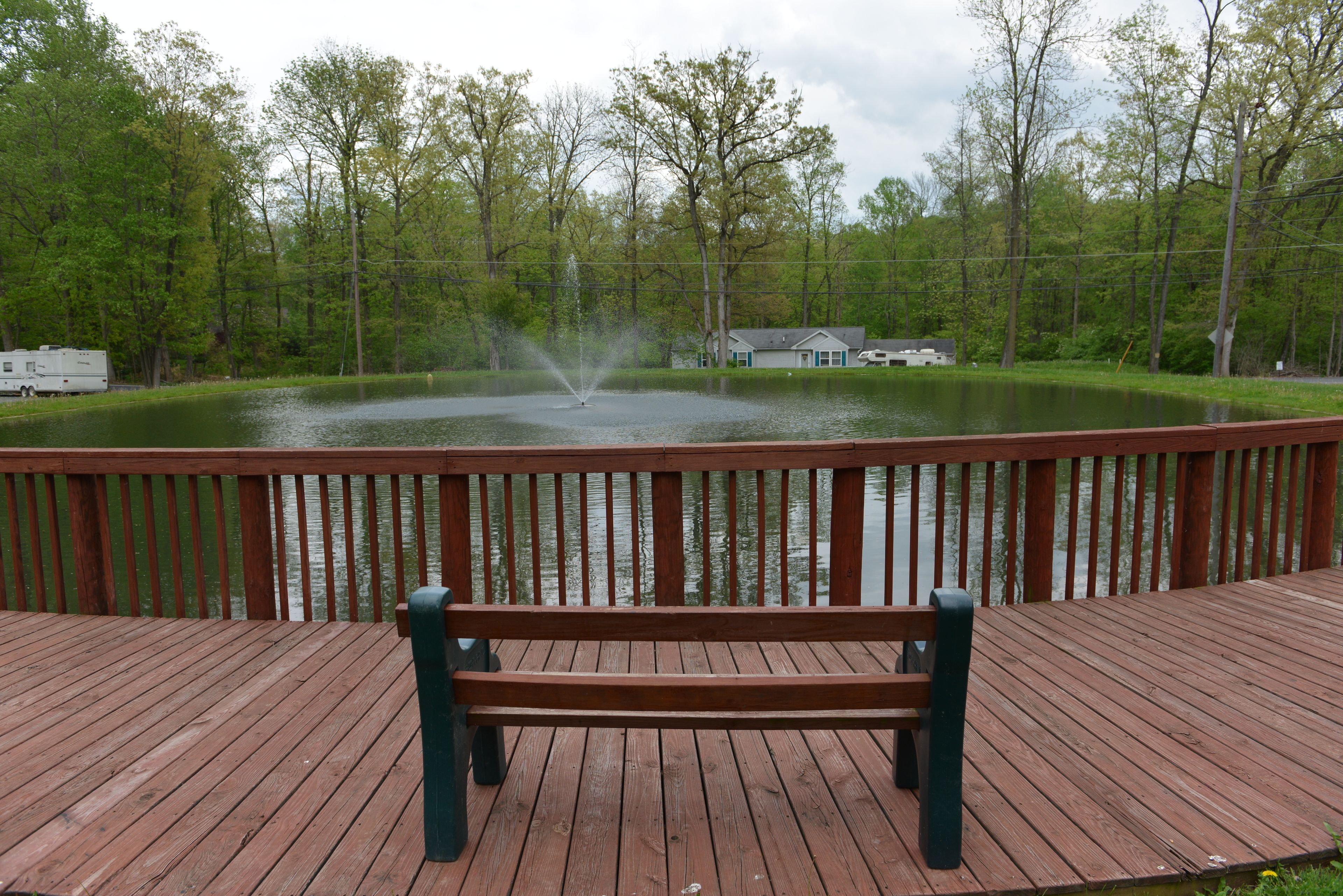 Une terrasse en bois avec un banc donnant sur un étang, et une maison en arrière-plan.