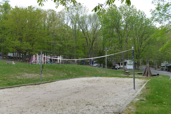 A sandy volleyball court with a net, surrounded by trees and a picnic area. - Sun Valley Camping and RV Resort (Narvon)