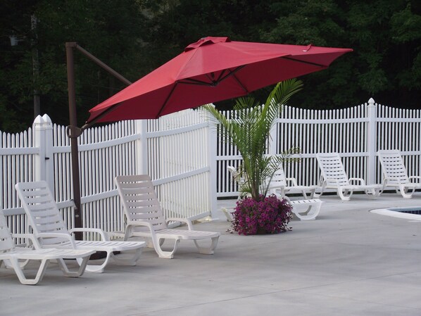 A poolside area with white lounge chairs and a red umbrella. - Sun Valley Camping and RV Resort (Narvon)